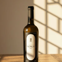 A bottle of Nomos Trajadura 2022 white wine with a label that includes the name 'Nomos' and the grape variety 'Trajadura'. The background is lightly patterned.